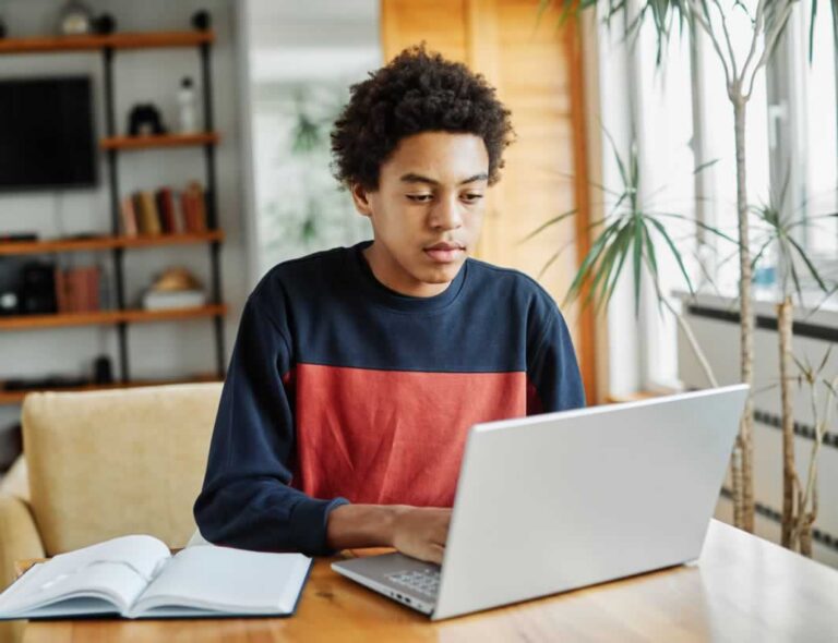 Teen boy working on laptop at table in home living room