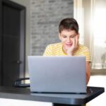 Teen boy looking at screen of laptop smiling
