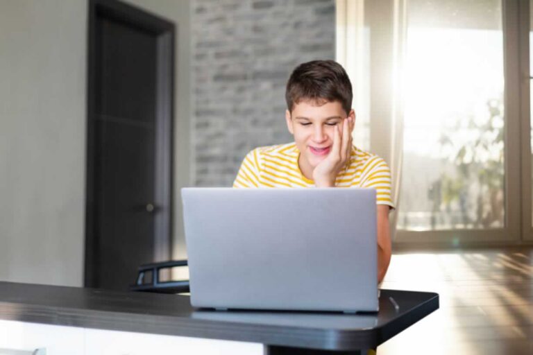 Teen boy looking at screen of laptop smiling