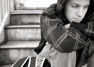 Teen boy sitting on step hunched with chin resting on knees experiencing youth loneliness