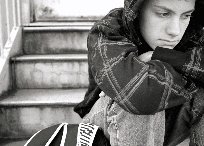 Teen boy sitting on step hunched with chin resting on knees experiencing youth loneliness