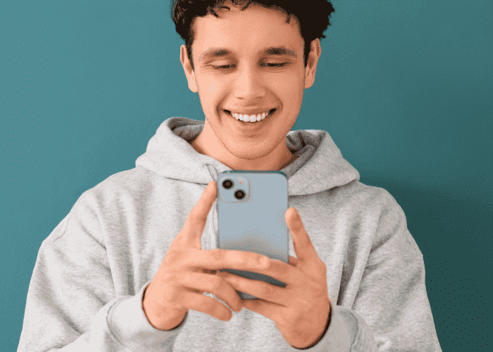 Teen boy looking at cellphone smiling after receiving support with how to use social media to improve teen mental health