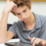 Teen boy using tablet with head in hand needing support with AI and teen mental health