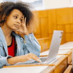 Teen girl sitting in classroom with laptop on desk needing support with digital literacy and teen mental health