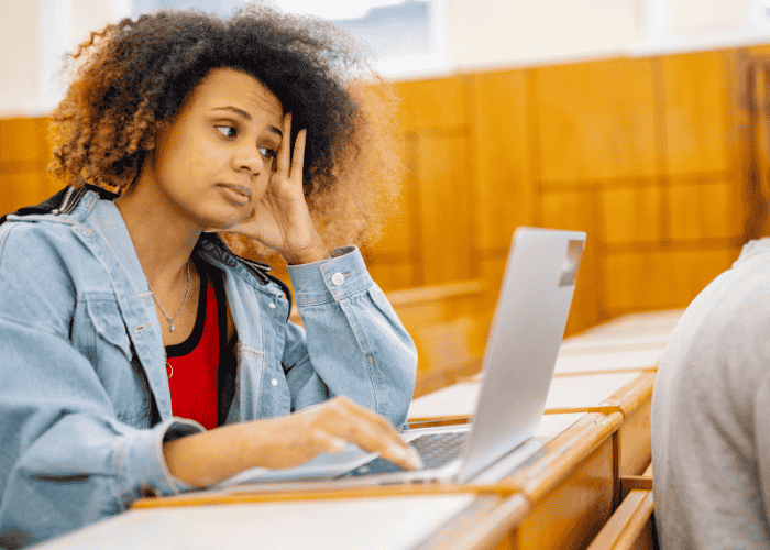 Teen girl sitting in classroom with laptop on desk needing support with digital literacy and teen mental health