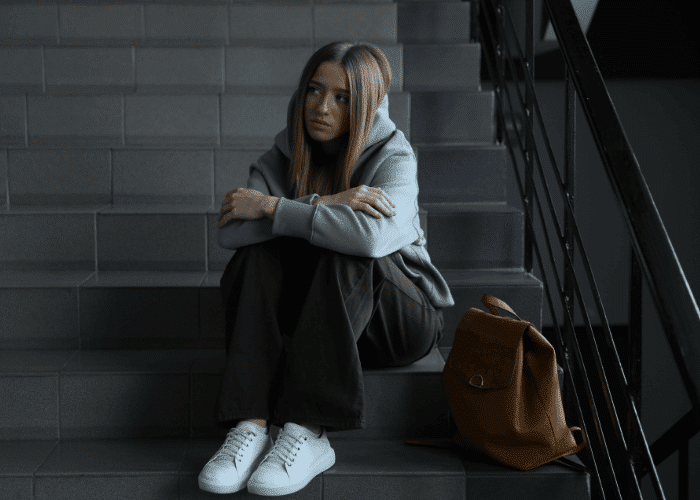 Teenage girl sitting on step with arms crossed and bag by feet needing crisis support for California teens