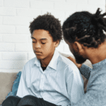 Dad sitting with teenage boy on sofa illustrating how to talk to your teenager about mental health