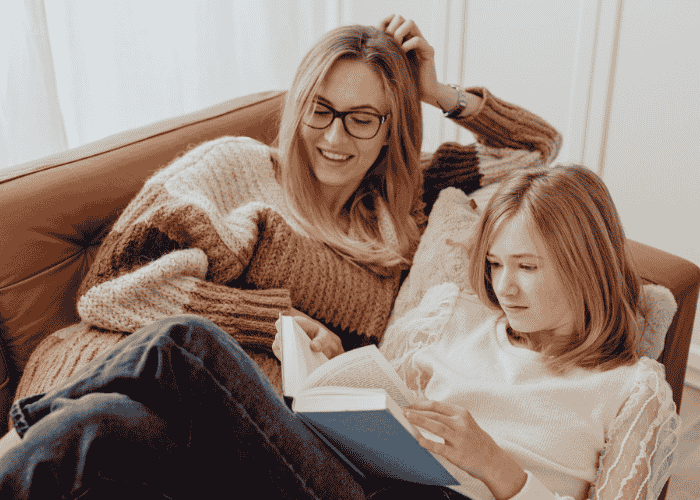 Teenage girl and mom sitting on sofa together after support with how to keep communication open with a teen about mental health.