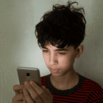 Teen boy looking at cell phone needing support with California teen digital safety