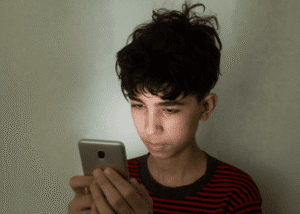 Teen boy looking at cell phone needing support with California teen digital safety