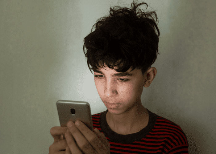 Teen boy looking at cell phone needing support with California teen digital safety