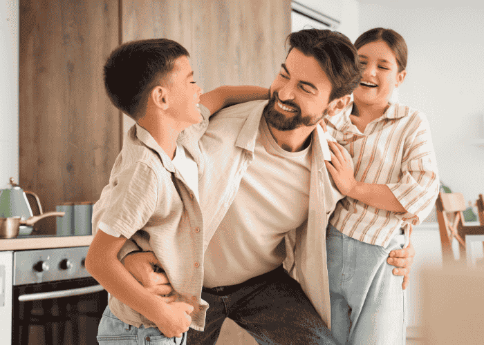 Dad hugging teen son and daughter playfully after seeking support with his parenting style. 