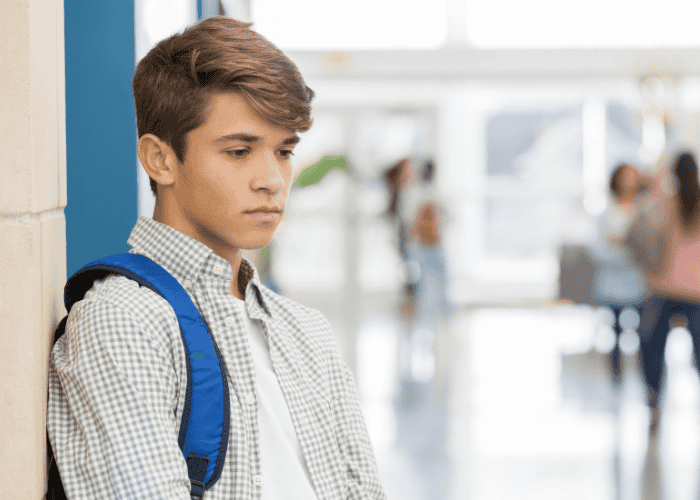 Teen boy stood alone in school hallway experiencing rejection sensitive dysphoria