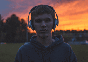 Teen boy outside wearing headphones with sun setting behind him needing support with downside to resilience in teen mental health