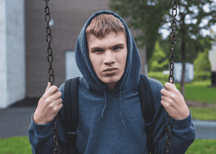 Teen boy sitting on swing outside in park looking support with balancing safety vs. independence in treatment