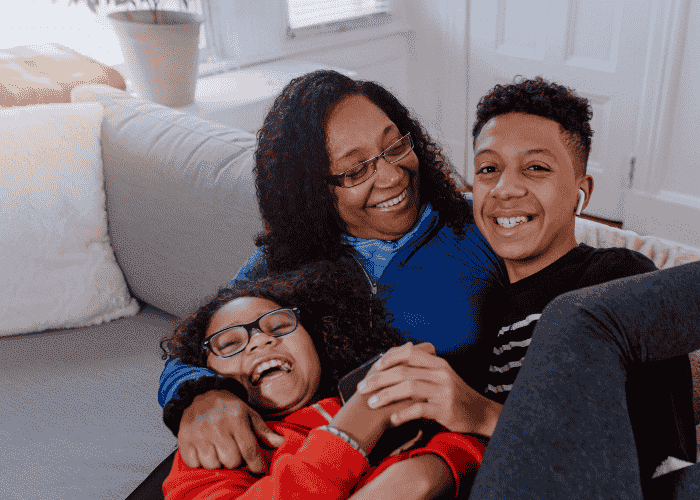 Teen mom on couch laughing with teen son and daughter after support with distance from home for teen treatment