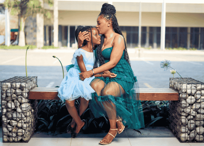 mom sitting on bench outside with teen daughter hugging her and kissing her on forehead after support with parent guilt