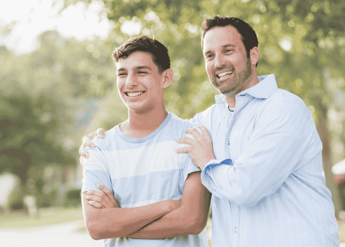 Dad outside with hands on shoulders of teen son smiling after support with red flags when choosing programs