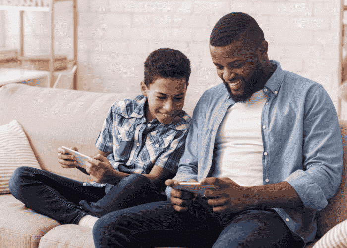 Dad with teen son playing on phones on couch smiling after support with second opinions before admission