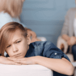 Teen boy leaning on arm of couch looking worried while parents discuss quality of residential treatment programs in background