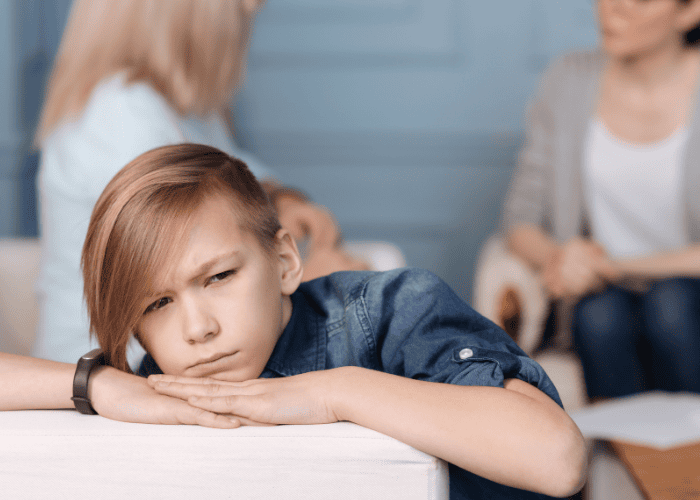 Teen boy leaning on arm of couch looking worried while parents discuss quality of residential treatment programs in background
