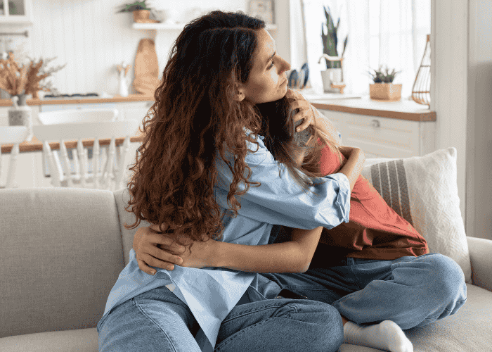 Mom hugging teen daughter on sofa needing support with how to pack for residential treatment