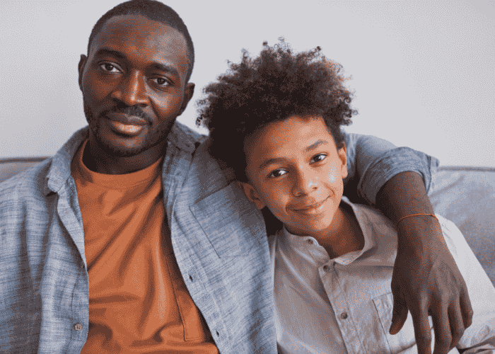 Dad sitting on couch with arm round teen son smiling after seeking support with talking to your teen about residential treatment