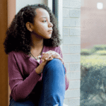 Young teen girl looking out window thinking about mental health treatment