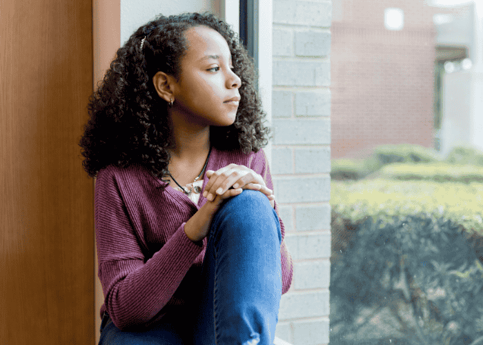 Young teen girl looking out window thinking about mental health treatment