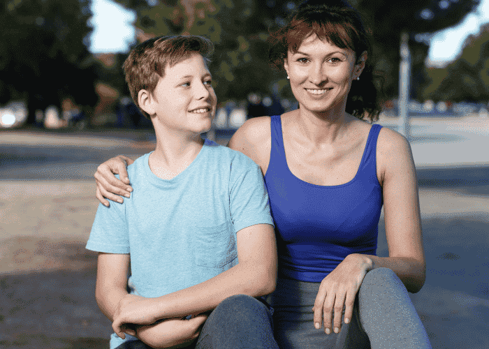Mom outside sitting with teen son smiling after support for raising resilient teens.