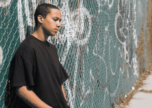 Teen boy leaning against wall outside alone wondering why are teens more connected but also more lonely