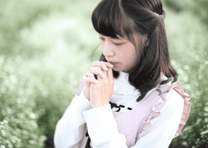 Teen girl standing in meadow with hands together in prayer needing support with faith vs clinical decision factors