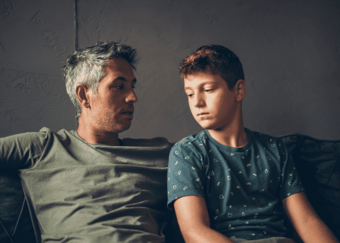 Father sitting with teen son on couch worrying about insurance vs private pay decisions