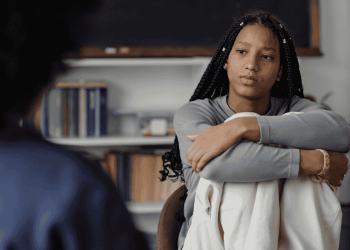 Teen in therapy session with legs pulled towards chest receiving support for teen navigating identity concerns. 