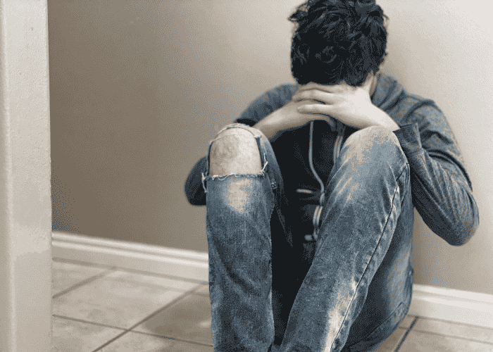 Boy sitting on the floor with head in hands in need of support with gender identity exploration in teens