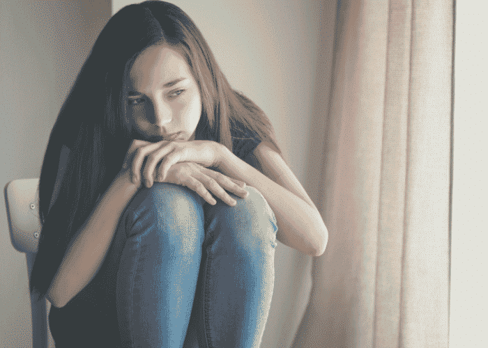 Teenage girl curled up on a chair before Long-Term Self-Concept Outcomes