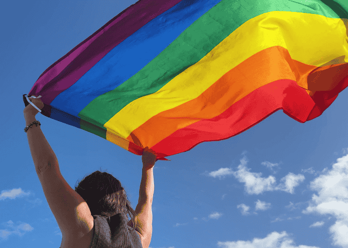 Teen girl holding pride flag above shoulders after support with LGBTQ+ teen mental health