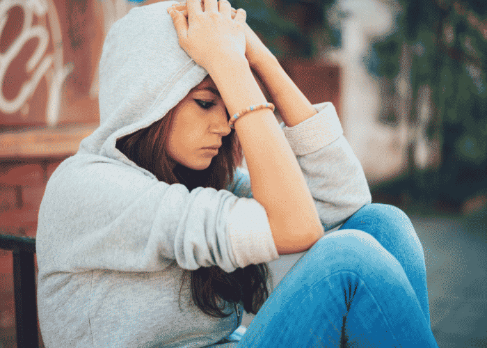 Teenage girl sitting on the sidewalk with hands on head before Intensive outpatient therapy