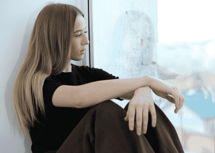 Sad teenage girl looking out the window struggling with creative identity expression in teens