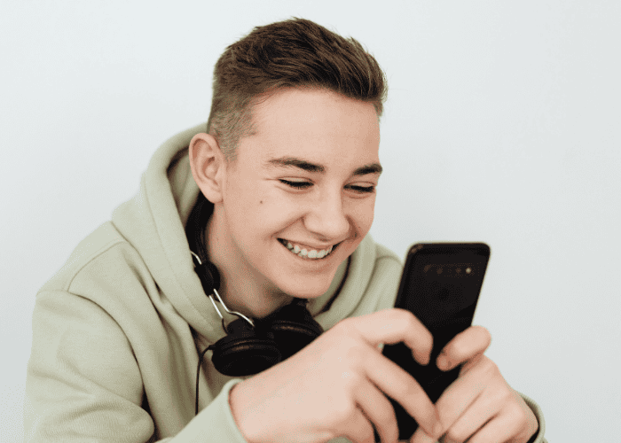 Teenage boy smiling at phone after learning the signs of online grooming