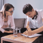 Teenage boy sitting next to adult at small table writing during Resilience Identity Development training