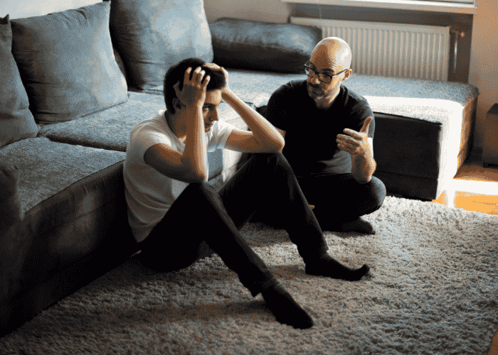 Teenage boy with his hands on his head, with parent figuring out how to explain residential treatment to your teen