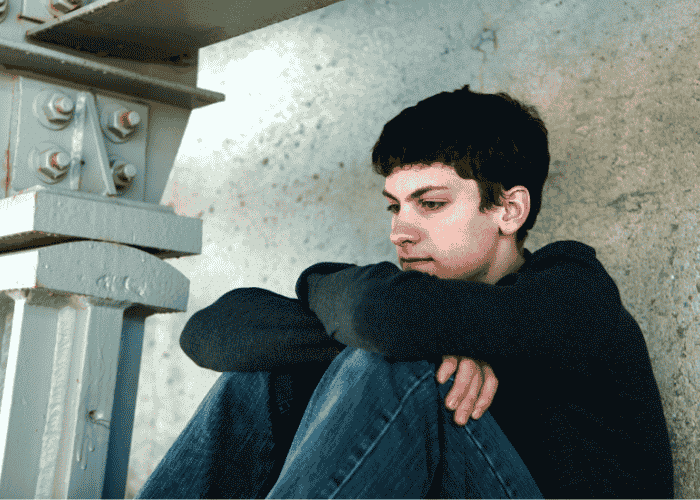 Teenage boy with his knees to his chest struggling with regression after residential treatment