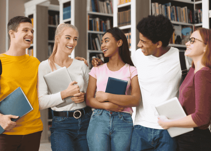 Group of teens in library holding books and smiling after support with stigma in teens.