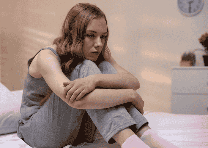 Teen girl sitting on bed with knees pulled to chest wondering about building confidence after treatment