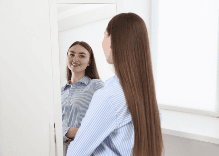 Teenage girl looking at herself happily in the mirror after receiving treatment for body dysmorphia in teens