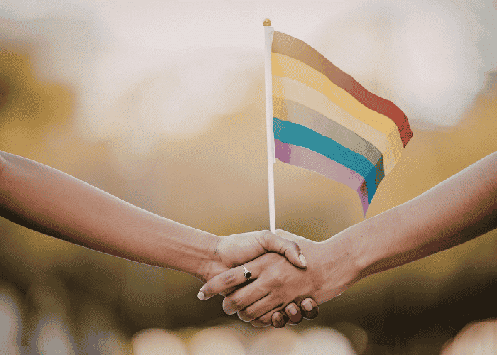 Two hands holding a LGBTQ+ flag needing after LGBTQ+ affirming therapy
