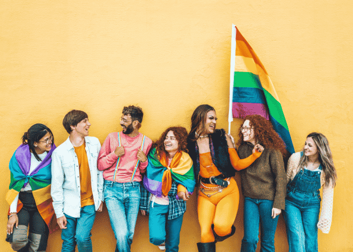 Teens leaning against wall holding LGBTQ+ flags after LGBTQ+ affirming therapy