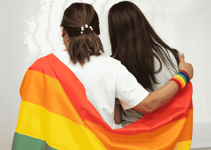 Two teen girls with Pride flag around shoulders after support with self-harm risks in LGBTQ+ teens