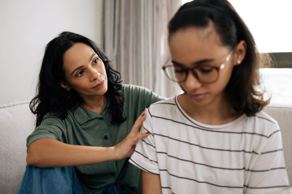 Mom sitting on couch next to daughter while offering support and holding her shoulder